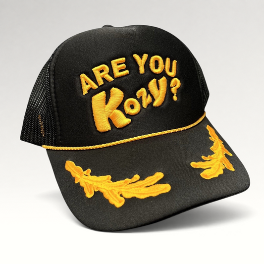 Raree Finds Are You Kozy? black trucker hat with gold raised embroidery, gold rope detail, and leaf bill accents.