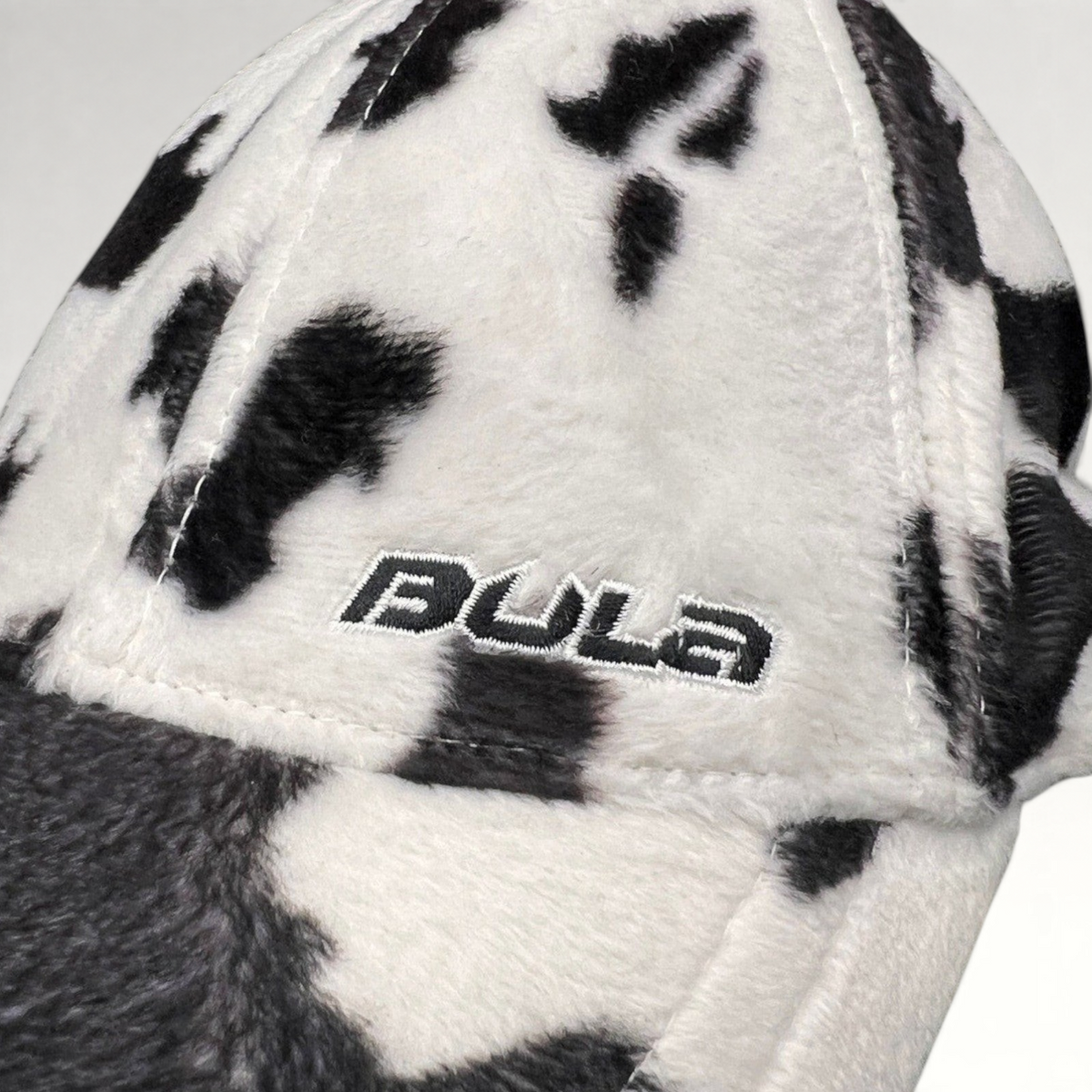 Raree Finds BULA black and white cow print plush fleece cap with embroidered side logo detail