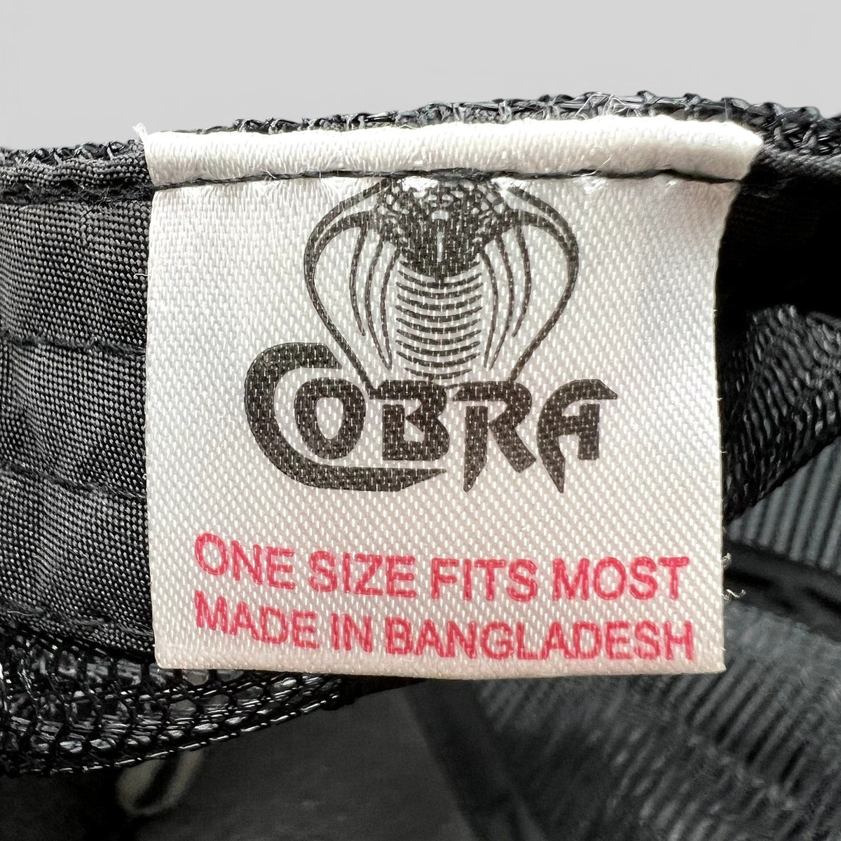 Raree Finds Cobra brand label inside a black trucker hat with white text and cobra logo, made in Bangladesh