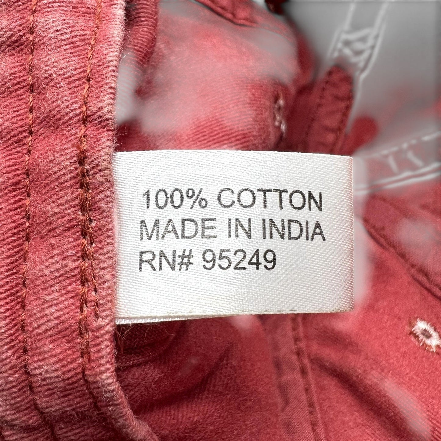 Raree Finds hat interior label showing 100 percent cotton material and made in India origin on distressed red fabric