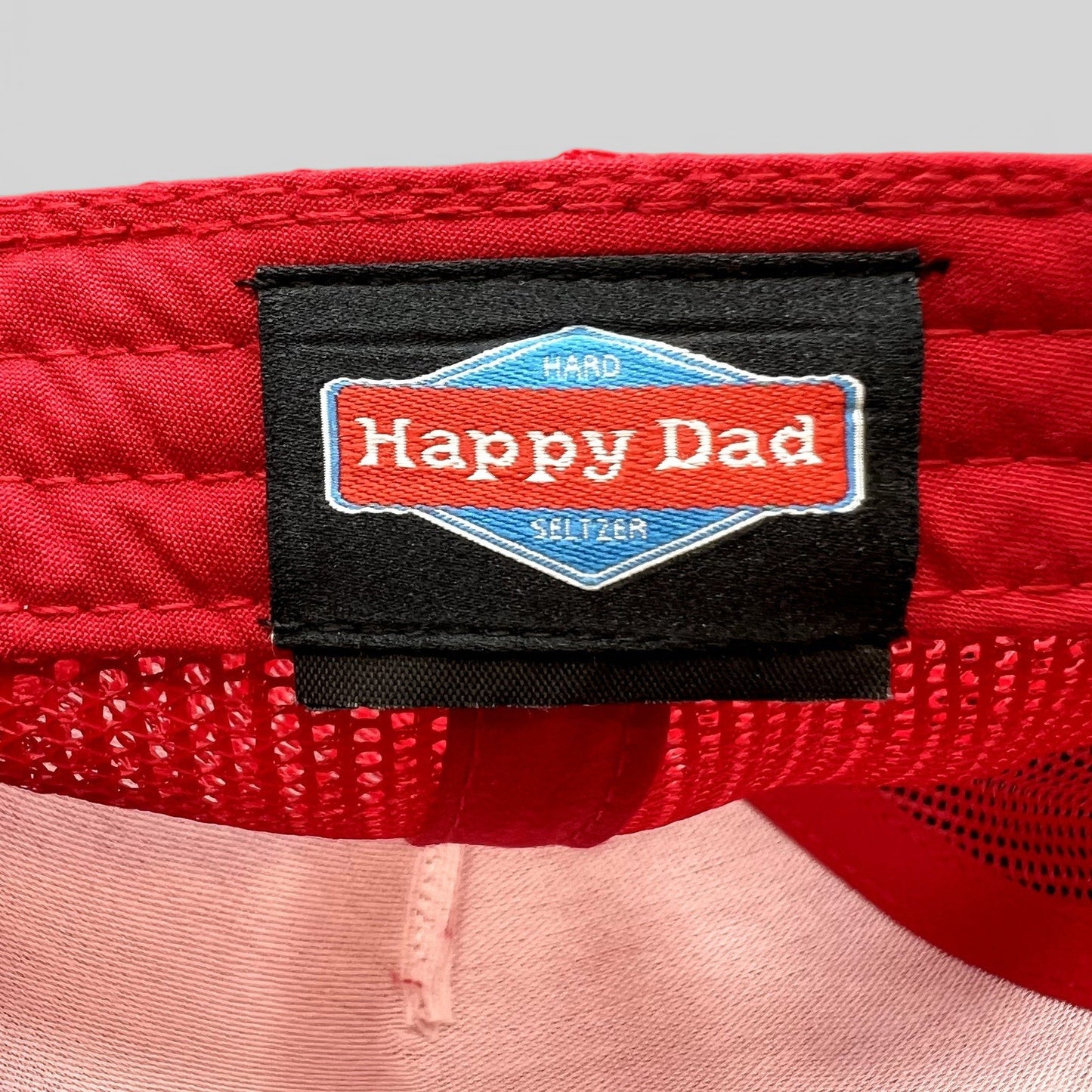 Raree Finds Happy Dad Hard Seltzer trucker hat interior label with brand logo on red mesh fabric