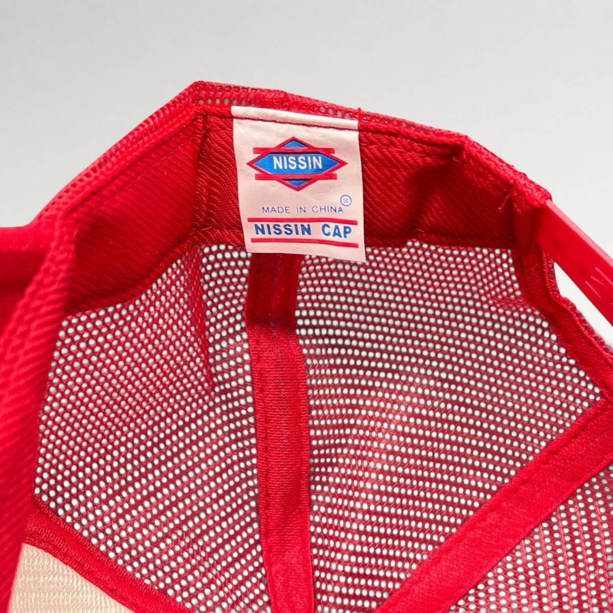 Raree Finds Nissin Cap red trucker hat interior label showing brand logo and mesh construction details