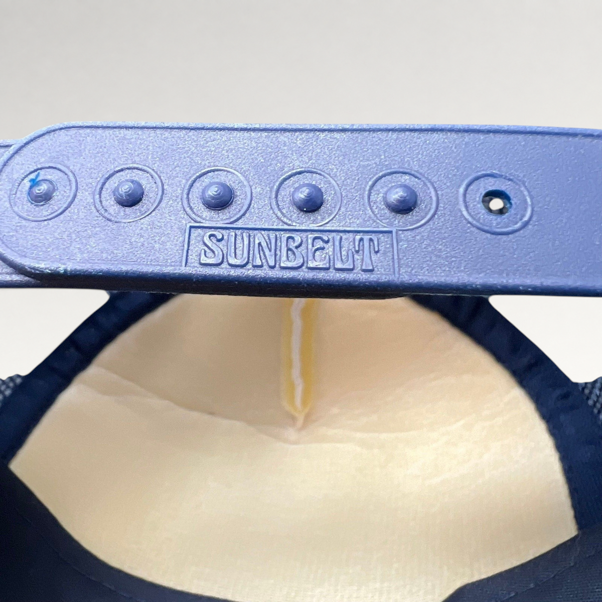 Raree Finds vintage Sunbelt snapback trucker hat showing the navy plastic adjustable strap with embossed logo