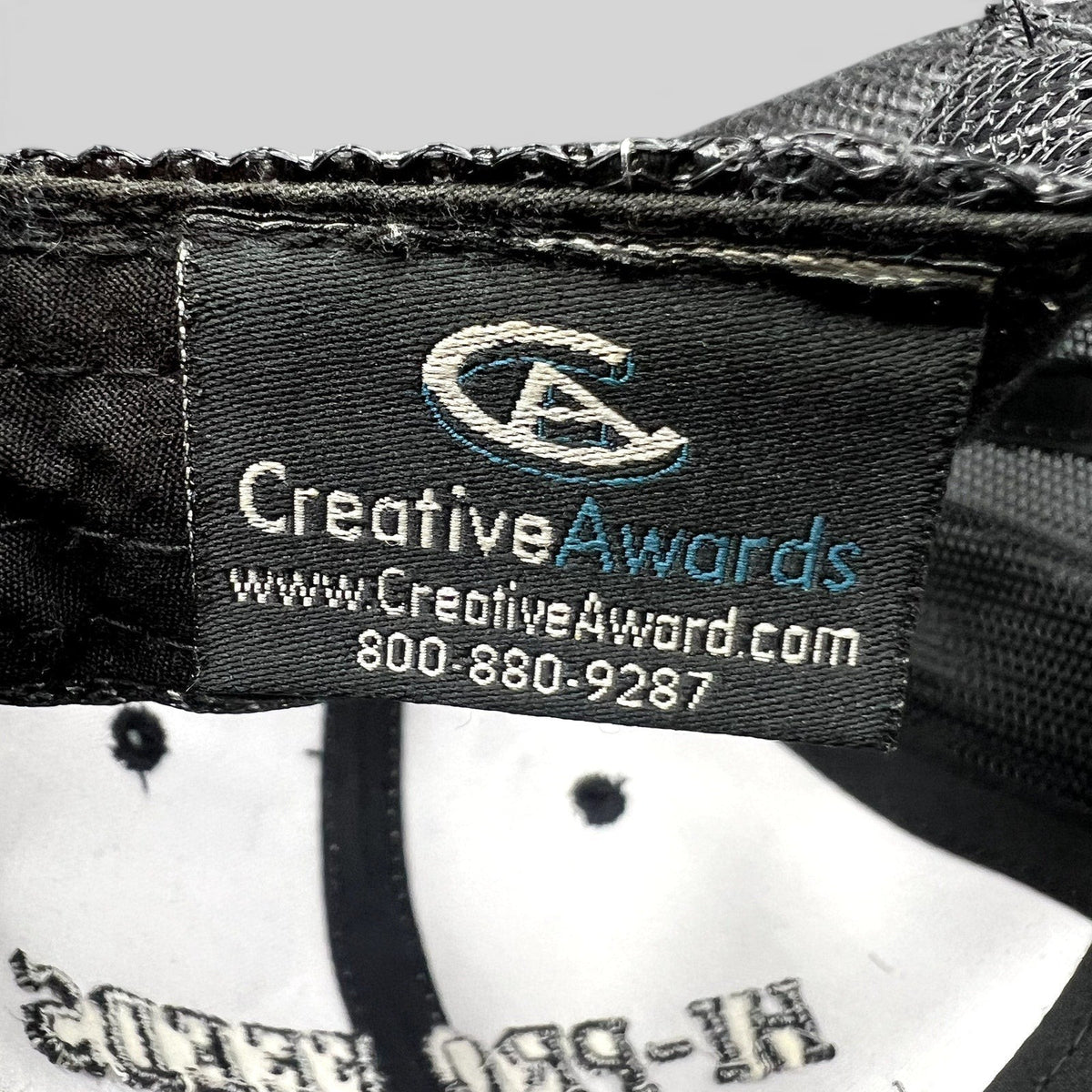 Raree Finds branded trucker hat interior tag showing Creative Awards manufacturer logo and contact information
