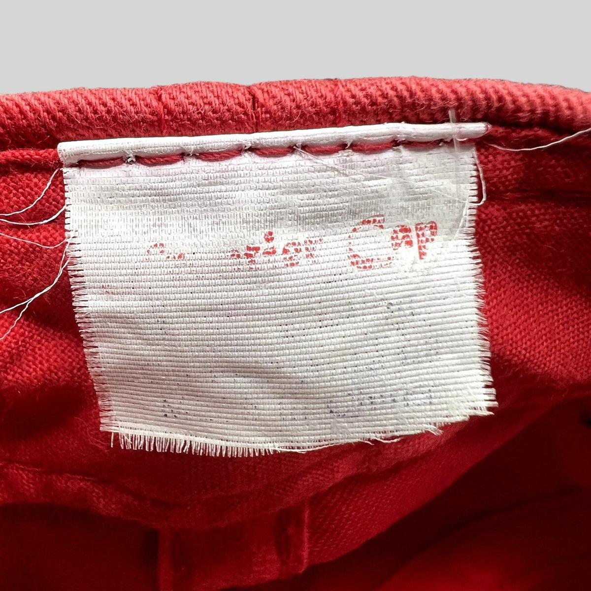 Raree Finds vintage Firestone Racing hat interior white fabric tag with faded red text on a red cotton background