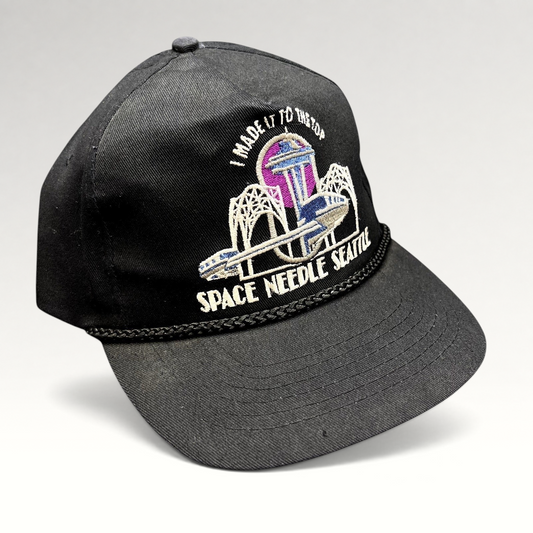 Raree Finds vintage 90s black snapback hat with embroidered Seattle Space Needle graphic and braided rope bill detail.