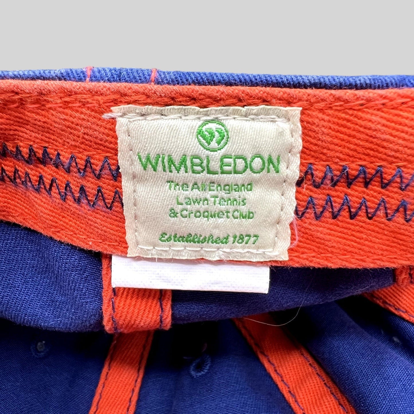 Raree Finds official Wimbledon tennis hat interior label with green logo and text on a navy and orange fabric cap