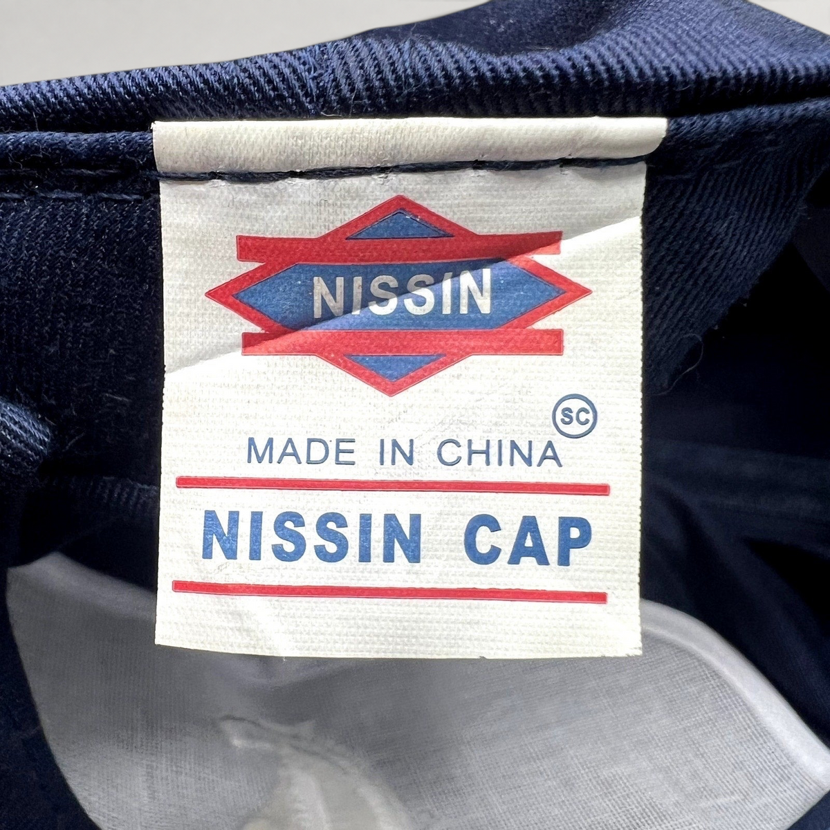 Raree Finds vintage Nissin Cap brand tag inside a navy blue promotional snapback hat