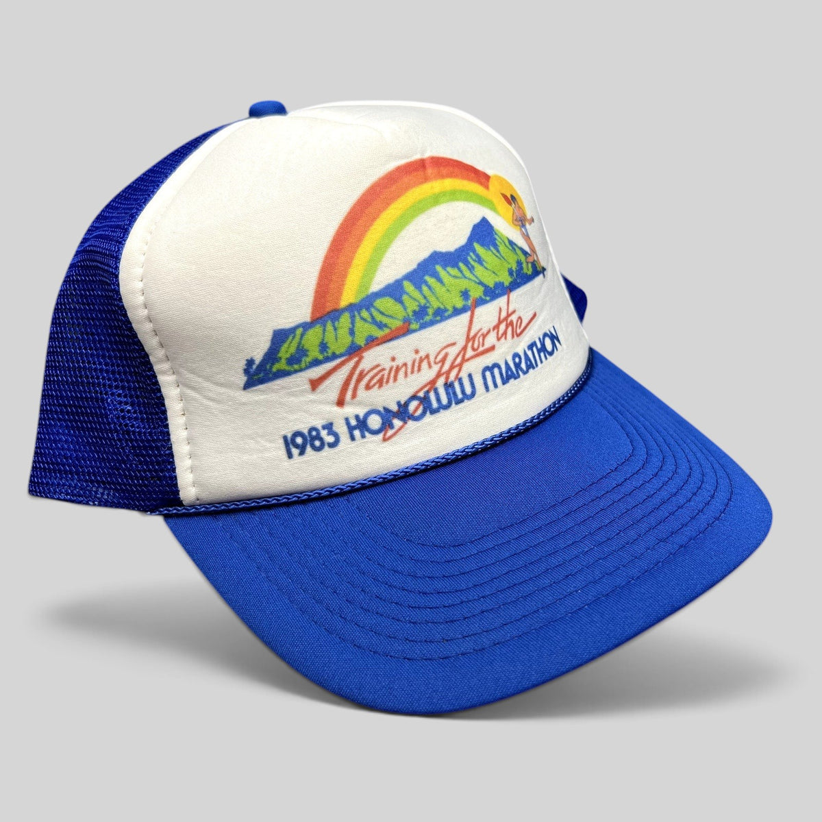Raree Finds vintage 1983 Honolulu Marathon trucker hat with white foam front, blue mesh back, and rainbow graphic.