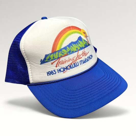 Raree Finds vintage 1983 Honolulu Marathon trucker hat with white foam front, blue mesh back, and rainbow graphic.