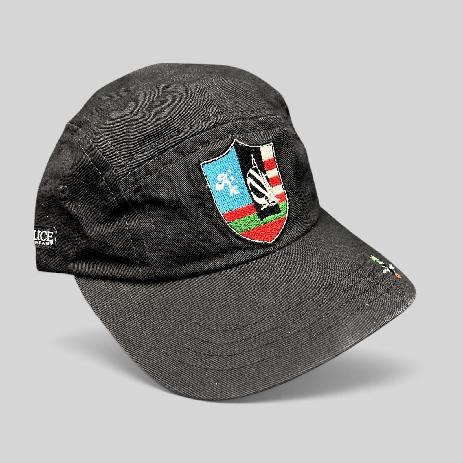 Raree Finds black Akomplice Clothing strapback hat with a colorful embroidered crest patch and mini brim graphic.