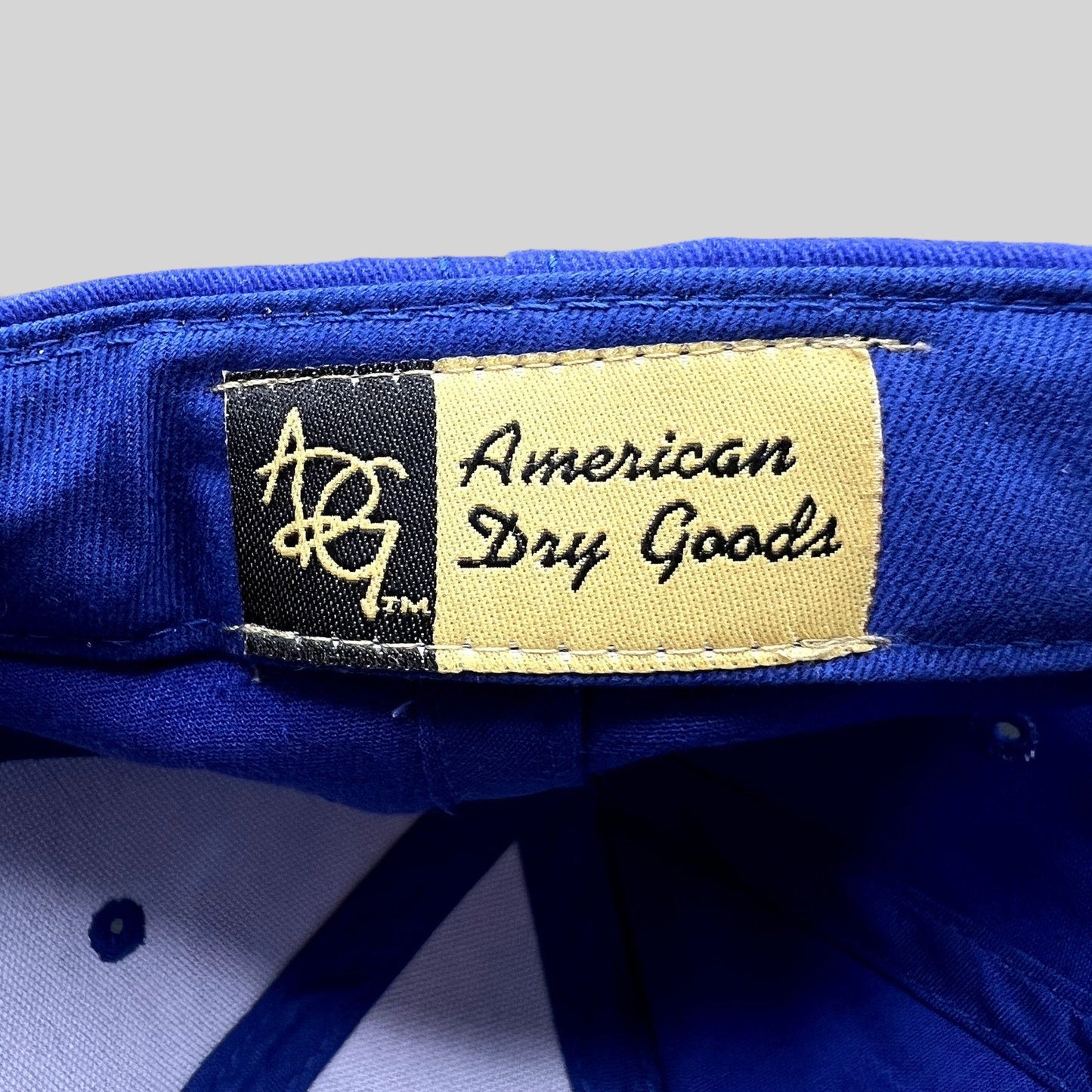 Raree Finds royal blue golf hat interior label featuring American Dry Goods branding on a cream and black tag.