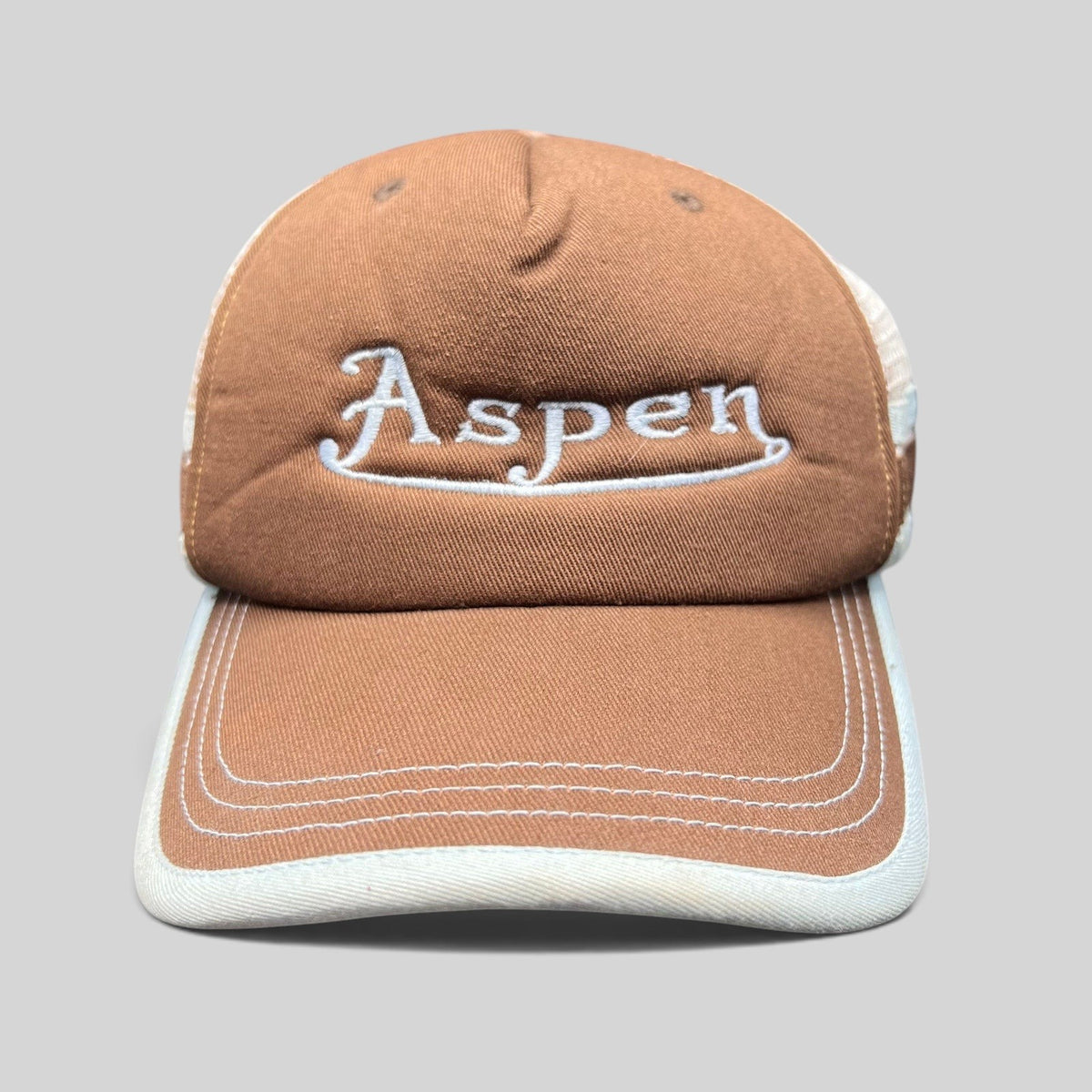 Raree Finds brown Aspen trucker hat with white script embroidery, mesh back, and contrast stitching on curved brim.