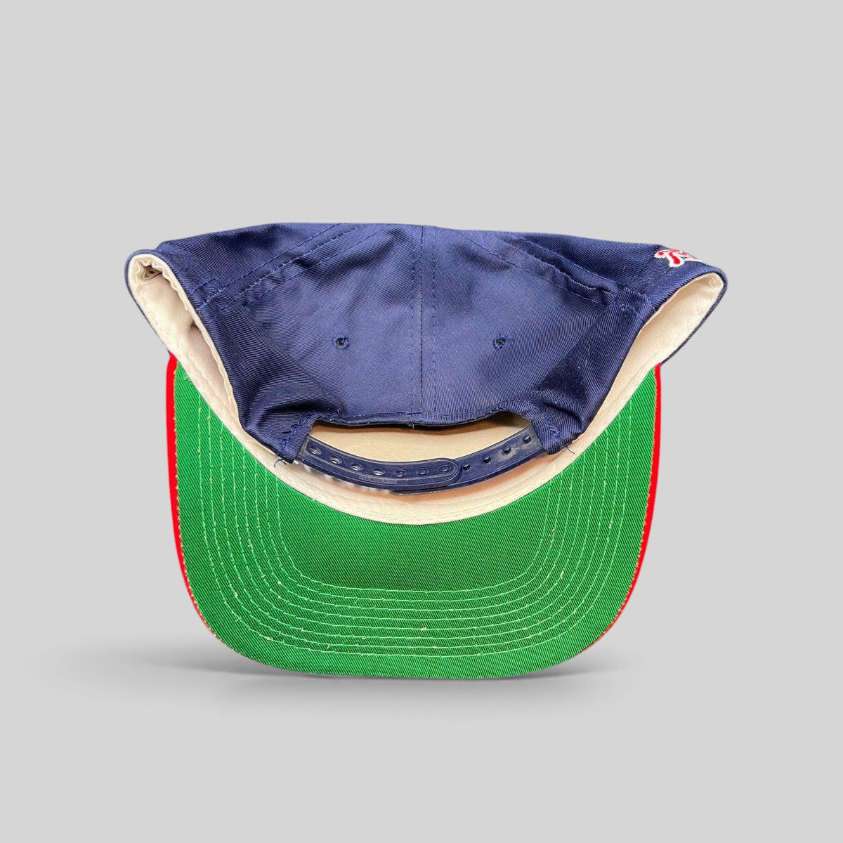 Raree Finds vintage 90s Atlanta Braves snapback hat showing the navy crown, red brim, and green underbrim from behind.