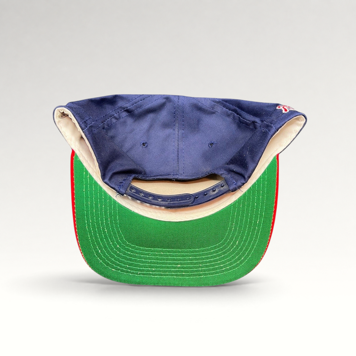 Raree Finds vintage 90s Atlanta Braves snapback hat showing the navy crown, red brim, and green underbrim from behind.