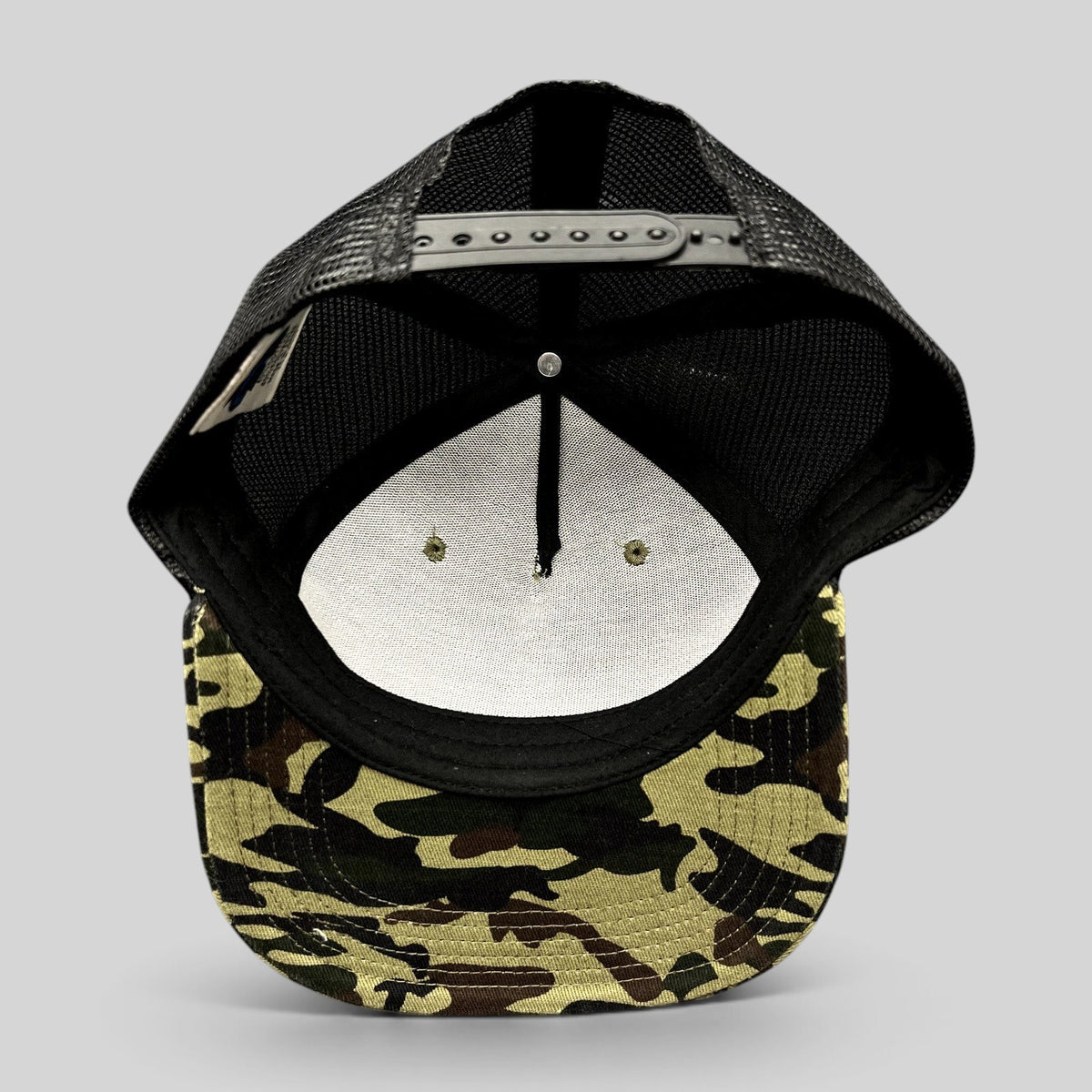 Raree Finds ATLWOOD woodland camo trucker hat showing the interior structure, black mesh back, and snapback closure.