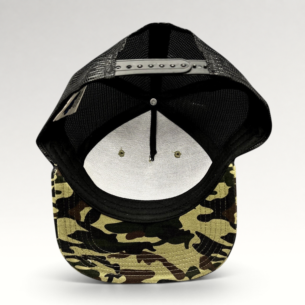 Raree Finds ATLWOOD woodland camo trucker hat showing the interior structure, black mesh back, and snapback closure.
