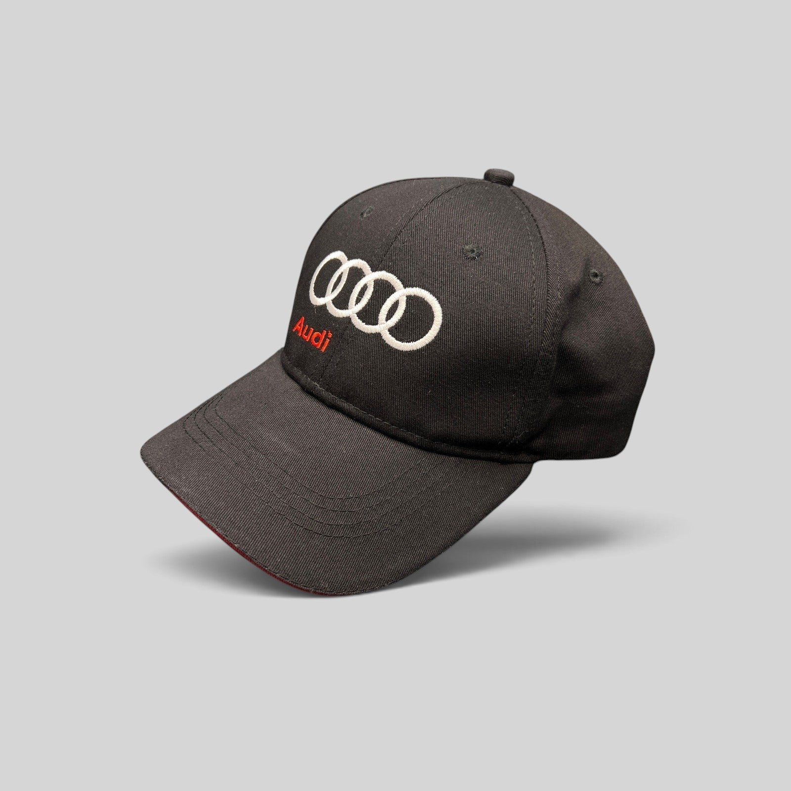 Raree Finds black cotton twill Audi strapback hat with white embroidered rings and red Audi logo on a dark background