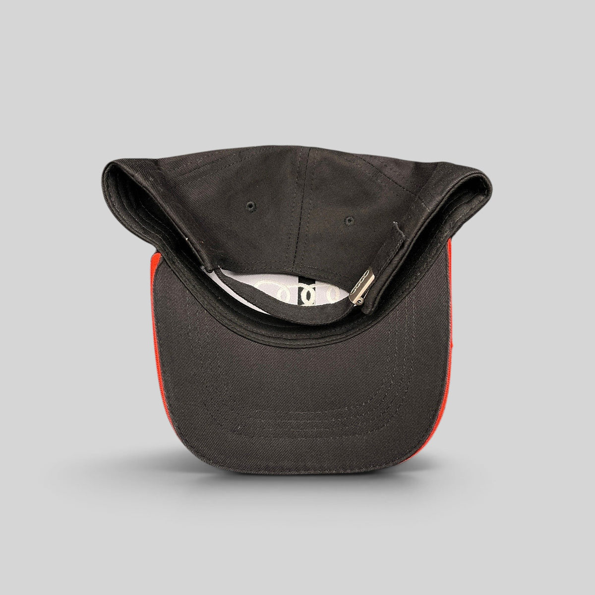 Raree Finds Audi black cotton twill strapback hat with red underbrim accent and metal clasp, top-down view.