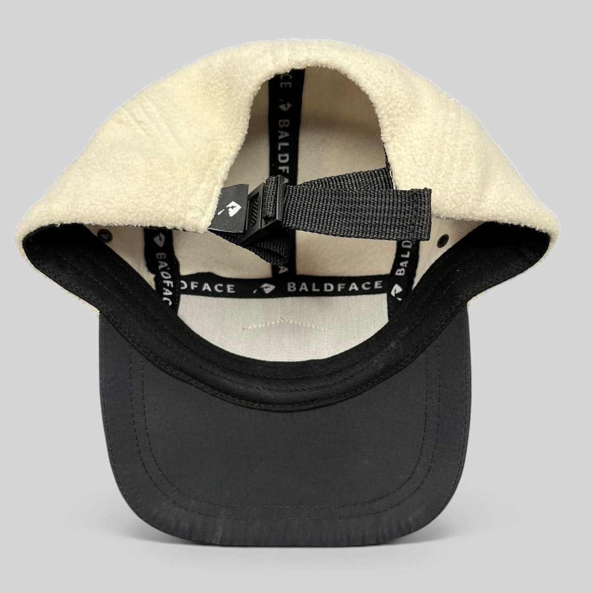 Raree Finds Baldface strapback hat featuring a cream fleece crown, black bill, and adjustable nylon clip closure.