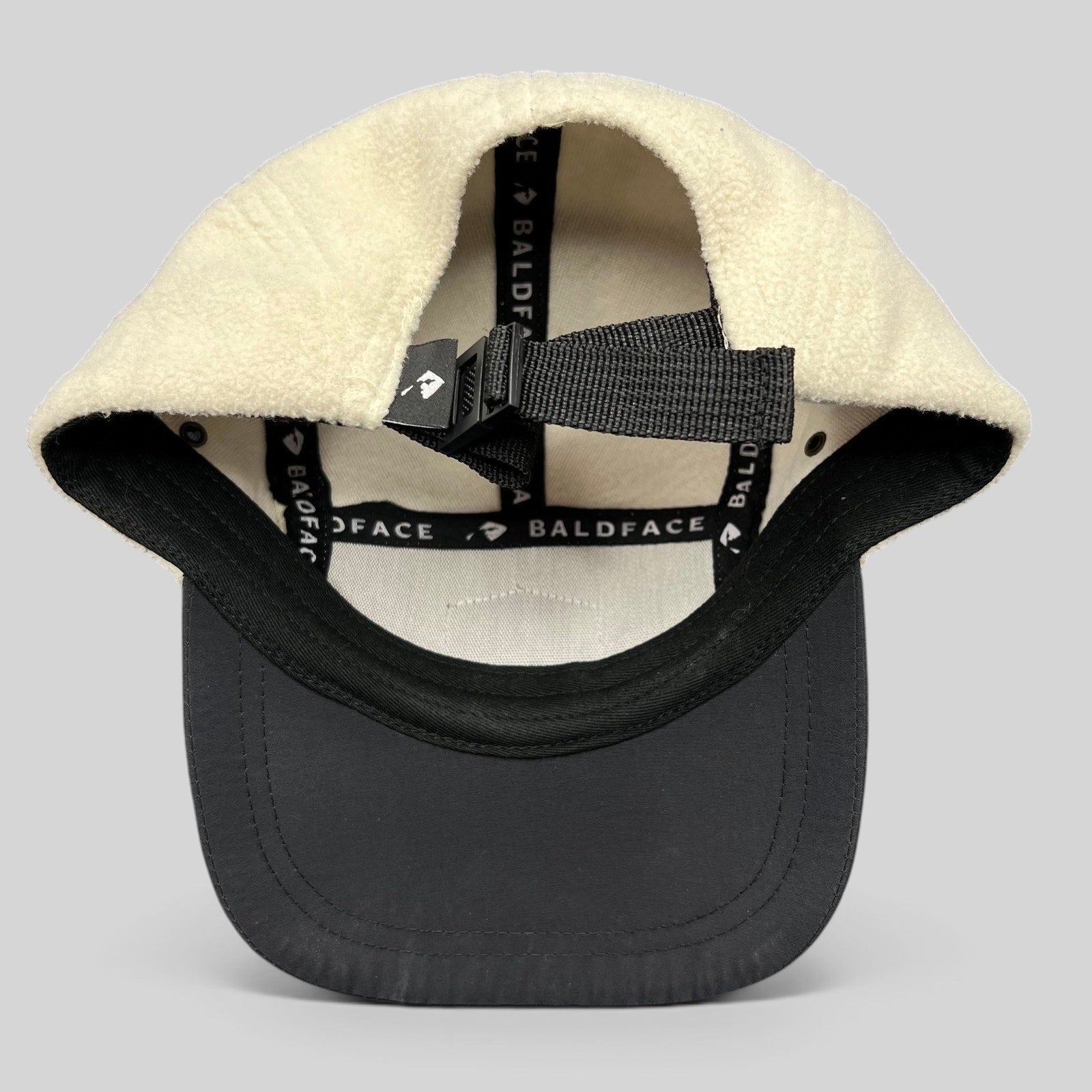 Raree Finds Baldface strapback hat featuring a cream fleece crown, black bill, and adjustable nylon clip closure.