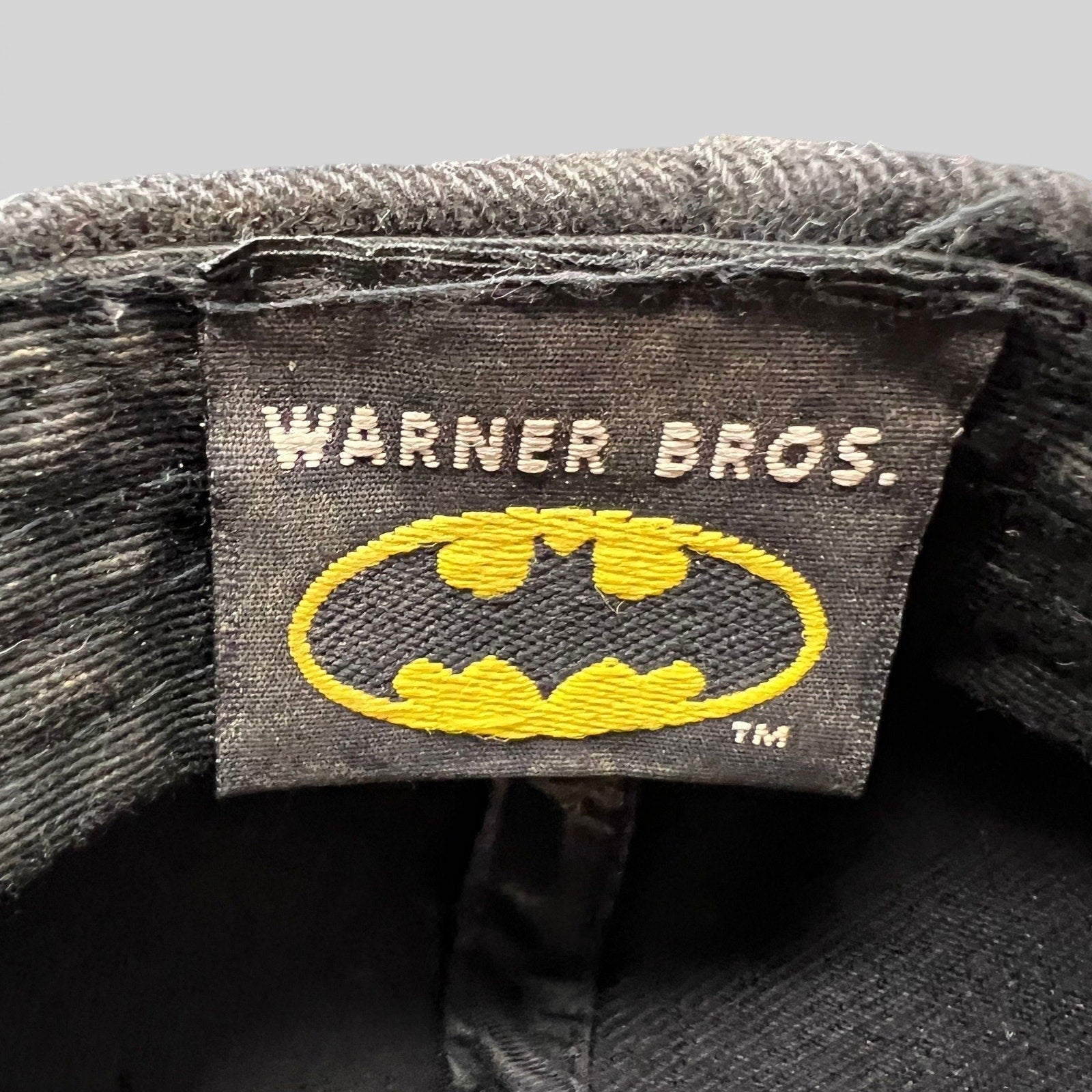 Raree Finds vintage Warner Bros Batman hat interior tag with yellow and black embroidered logo on black fabric