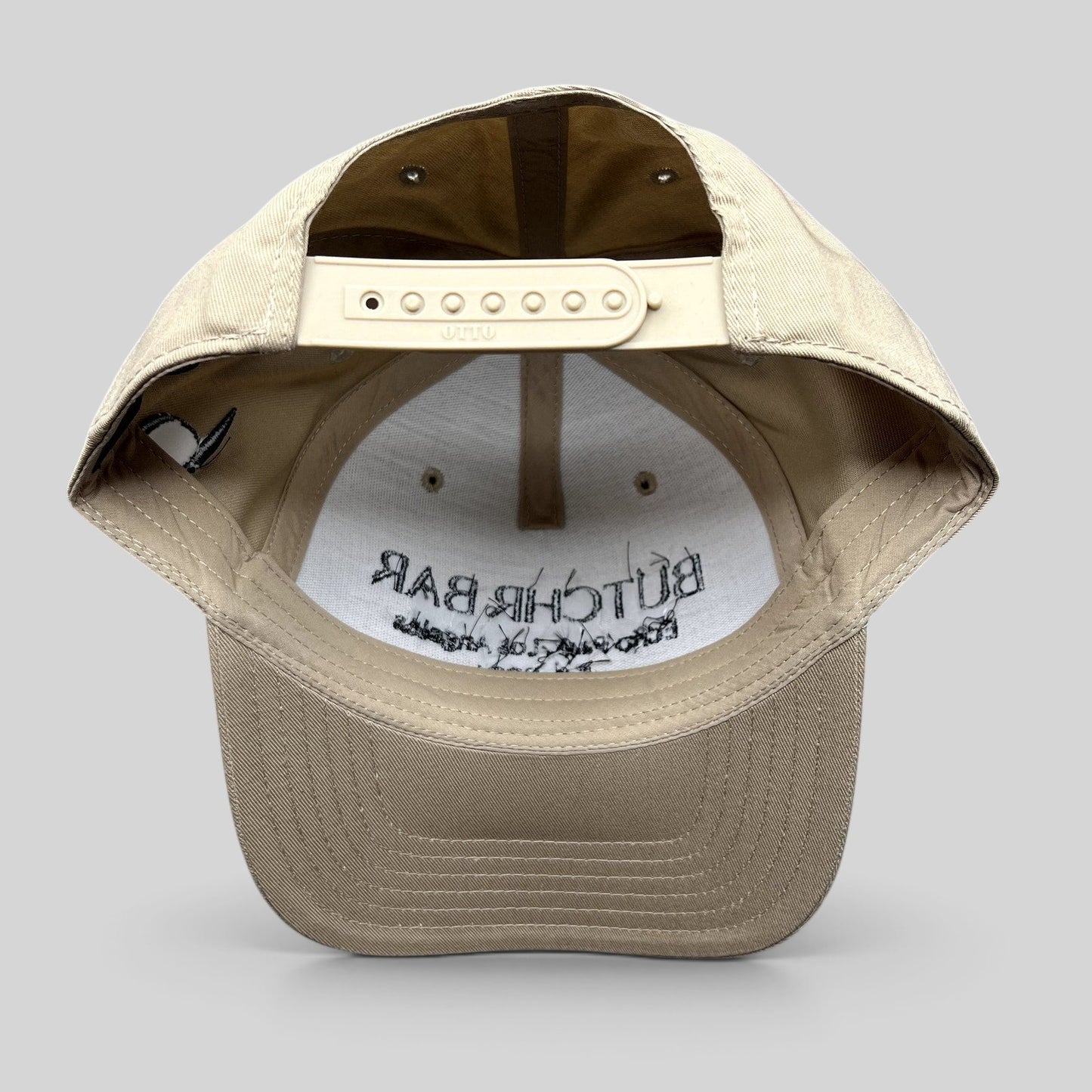 Raree Finds beige OTTO snapback hat showing the adjustable strap and interior branding of the BUTCHR BAR cap