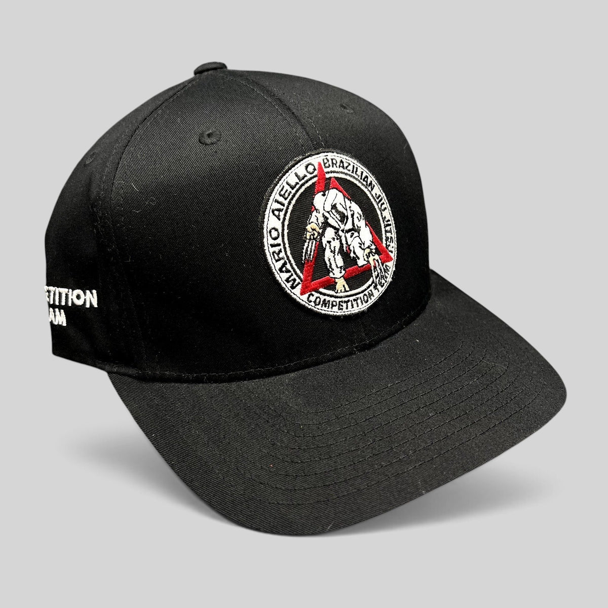 Raree Finds black Yupoong snapback hat with Mario Aiello BJJ competition team embroidered logo and side text.