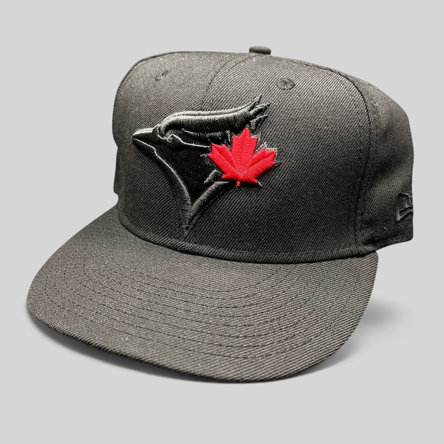 Raree Finds black New Era Toronto Blue Jays snapback hat with a tonal black logo and a vibrant red maple leaf detail.