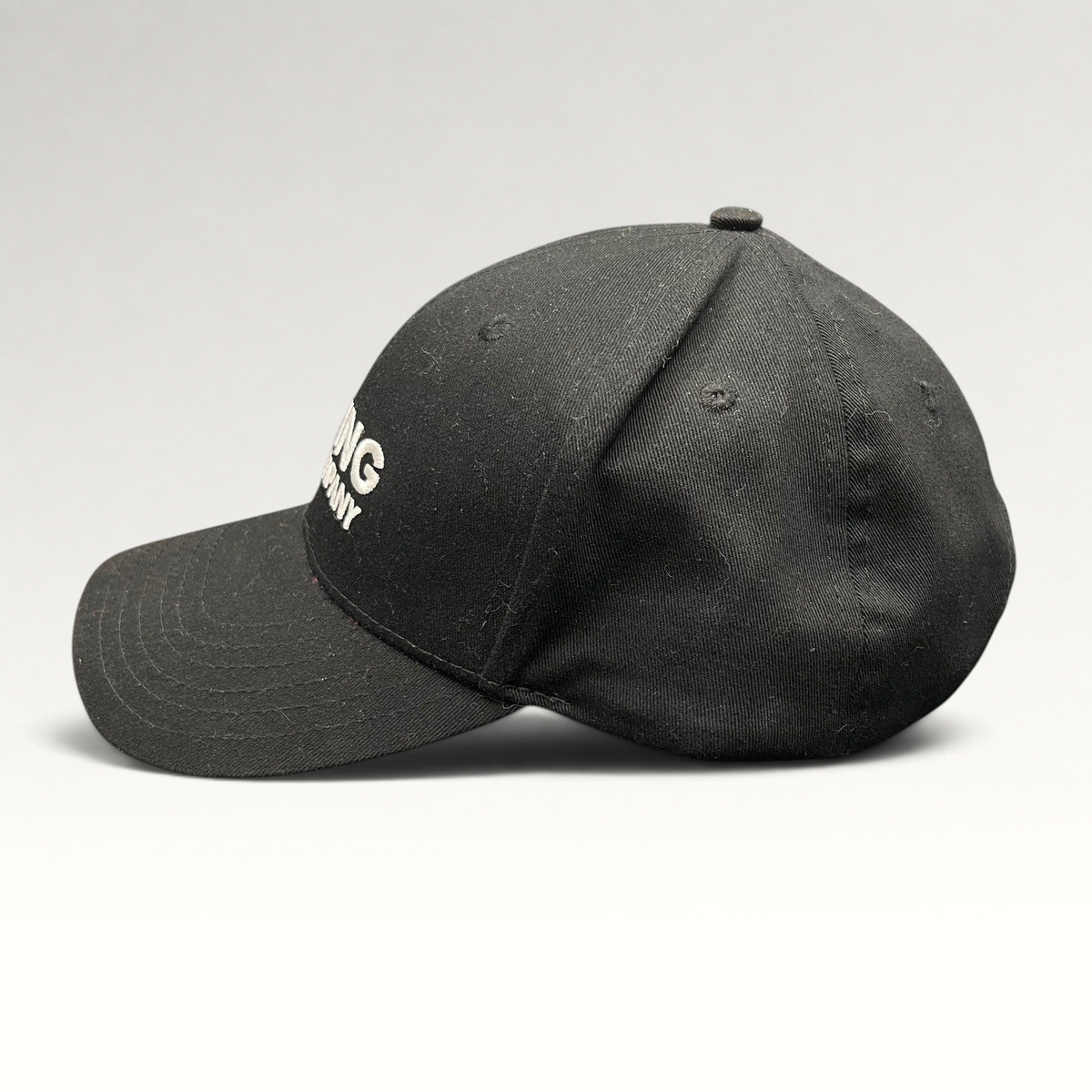 Raree Finds black The Boring Company strapback hat with white embroidered logo and curved brim, side profile view.