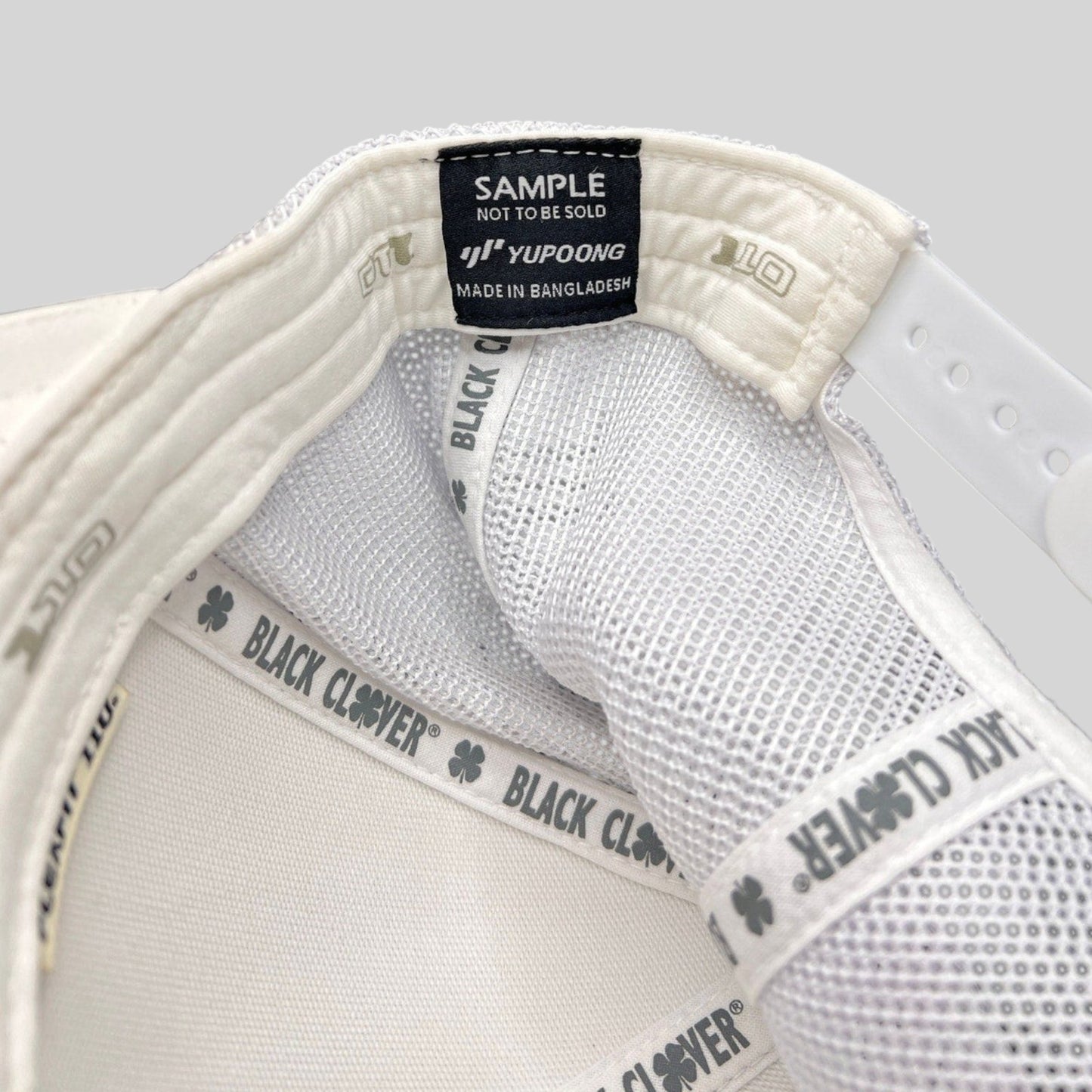 Raree Finds Black Clover Yupoong sample trucker hat interior showing white mesh and branded taping