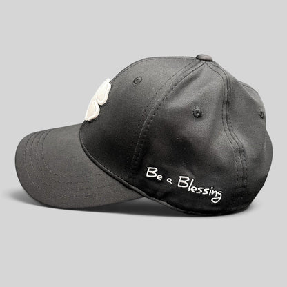 Raree Finds black snapback golf hat featuring a white clover logo and Be a Blessing embroidery on the side