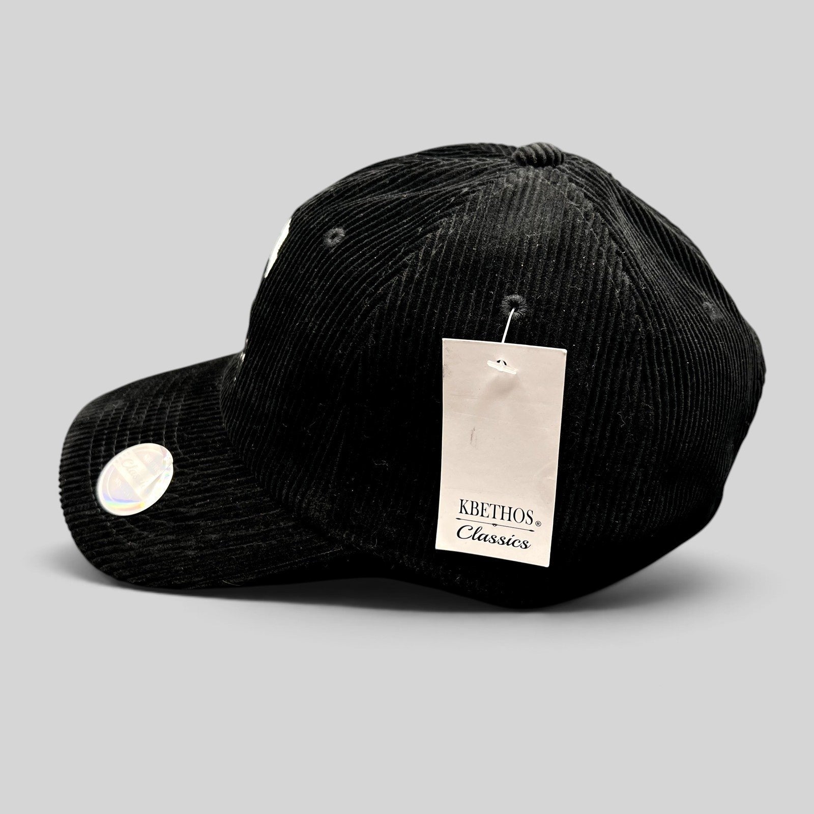 Raree Finds black corduroy strapback hat with KBETHOS Classics tag, featuring white embroidery and brass buckle.
