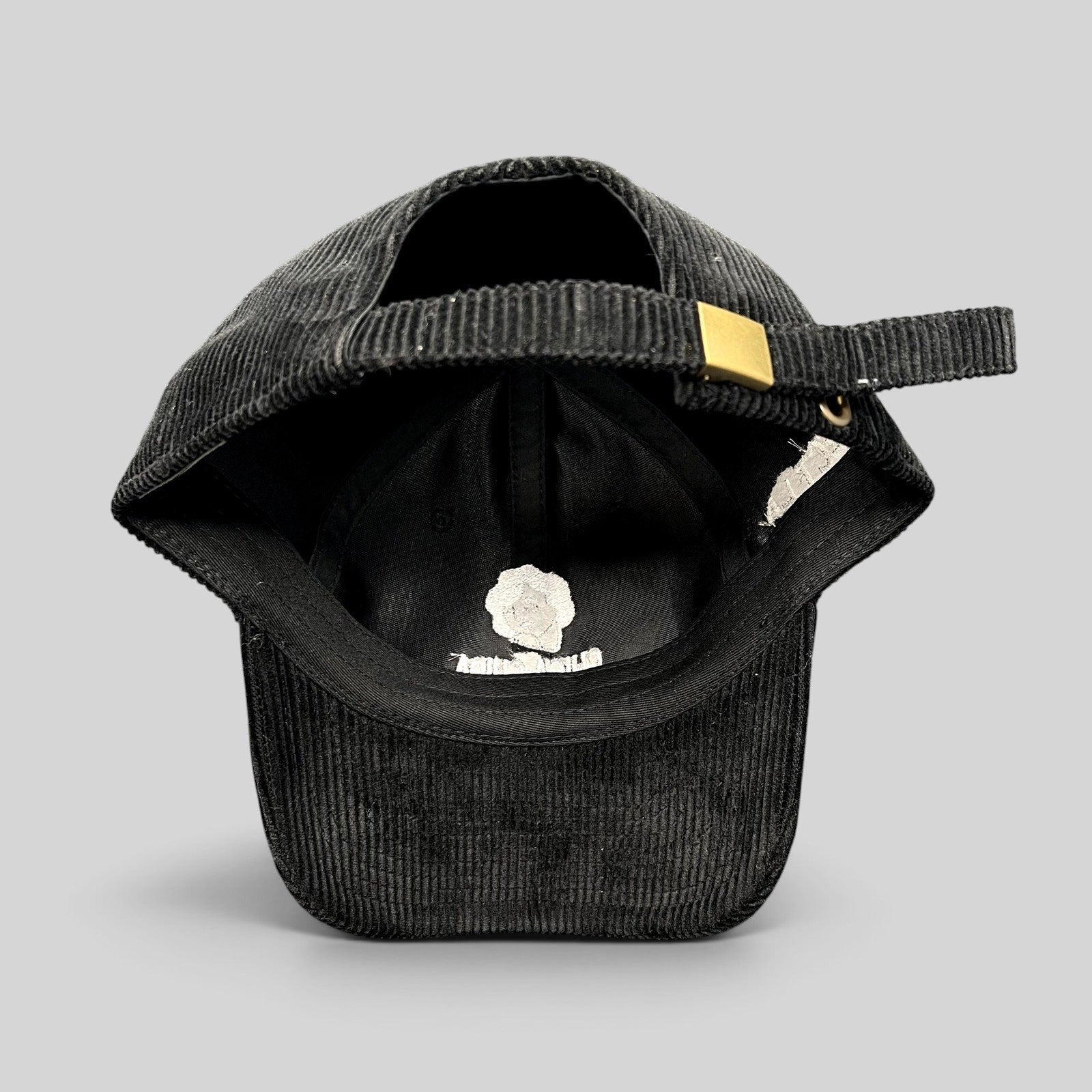 Raree Finds black corduroy strapback hat with brass buckle, showing the interior lining and adjustable strap detail.