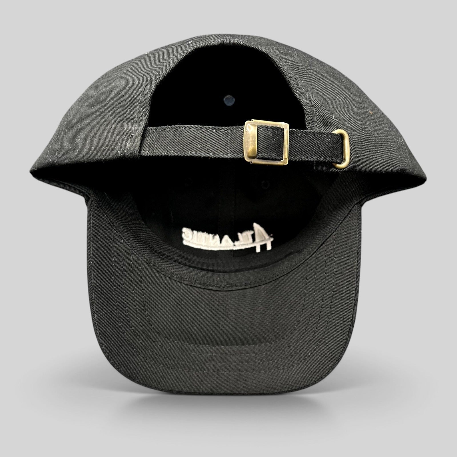 Raree Finds black cotton dad cap with adjustable strapback and brass buckle, showing interior script logo embroidery.