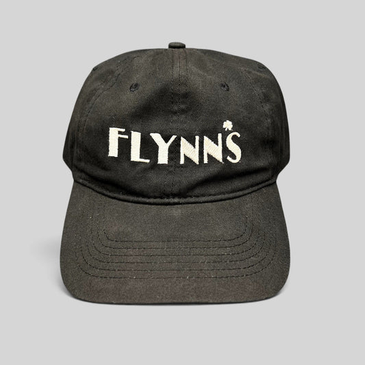 Raree Finds black unstructured strapback hat with white embroidered Flynn’s logo and shamrock accent on the front.