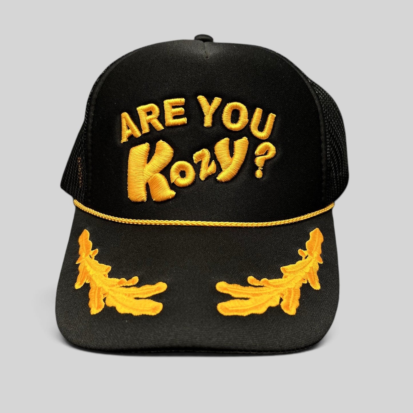 Raree Finds black trucker hat with gold Are You Kozy? raised embroidery, gold rope detail, and leaf bill accents.
