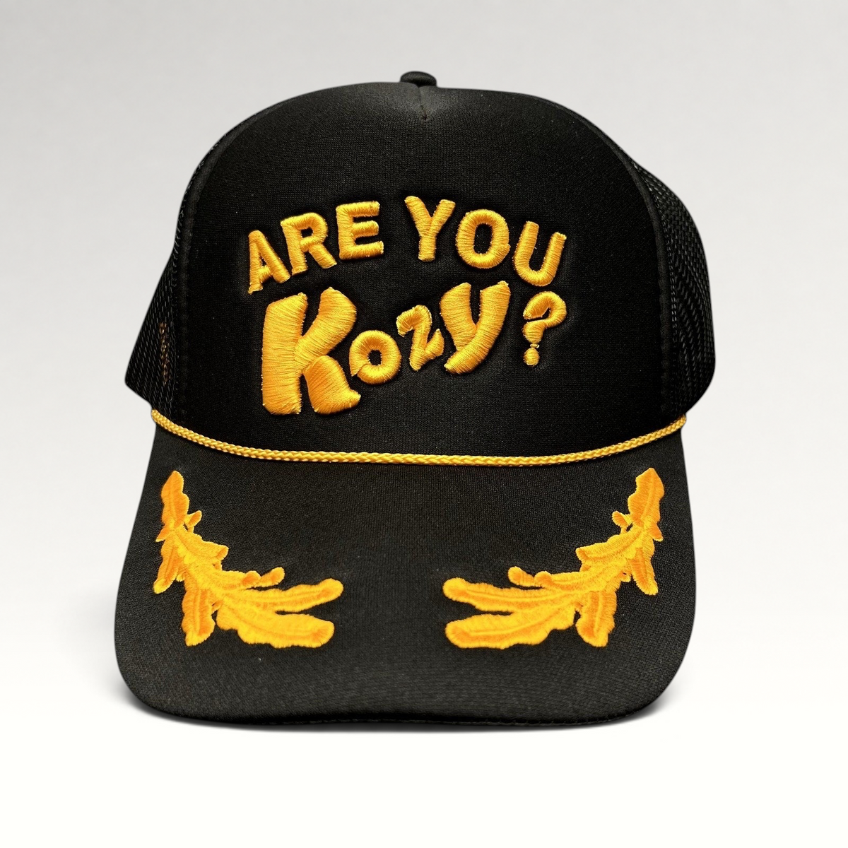 Raree Finds black trucker hat with gold Are You Kozy? raised embroidery, gold rope detail, and leaf bill accents.
