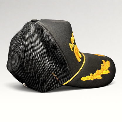 Raree Finds black and gold trucker hat with raised embroidery, gold rope detail, and leaf accents on the bill.
