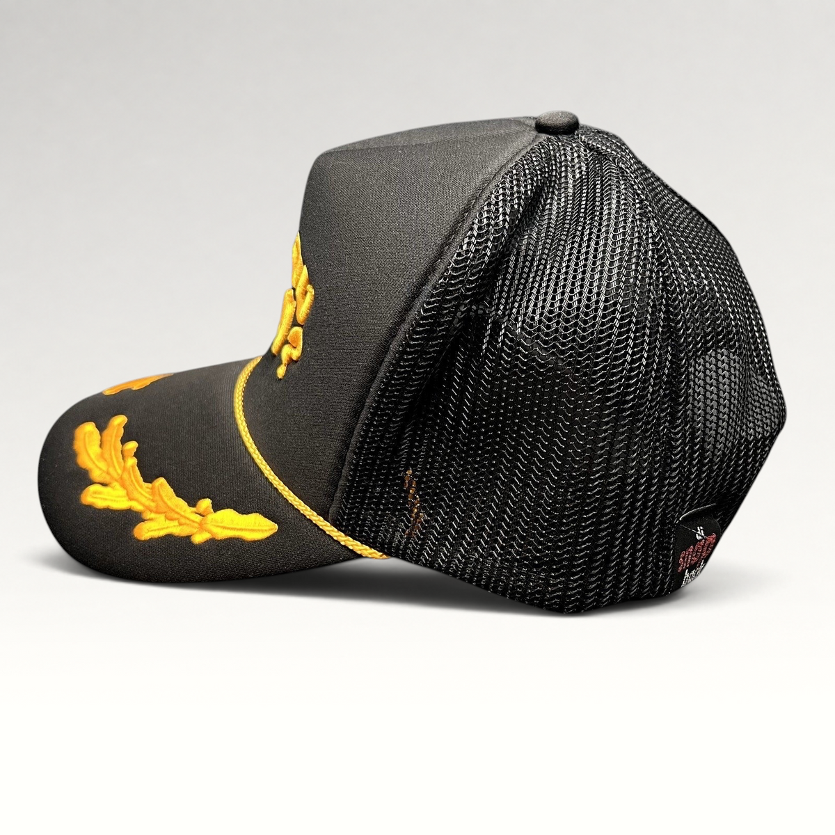 Raree Finds Are You Kozy? black trucker hat with gold embroidered leaf accents, rope detail, and mesh back panels.