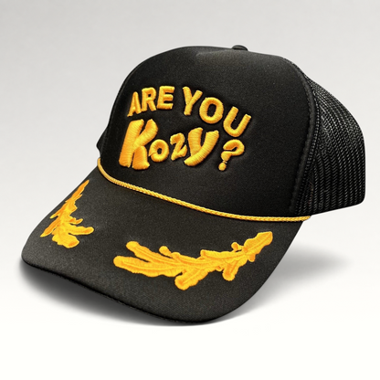 Raree Finds Are You Kozy? black trucker hat with gold raised embroidery, gold rope detail, and leaf bill accents.