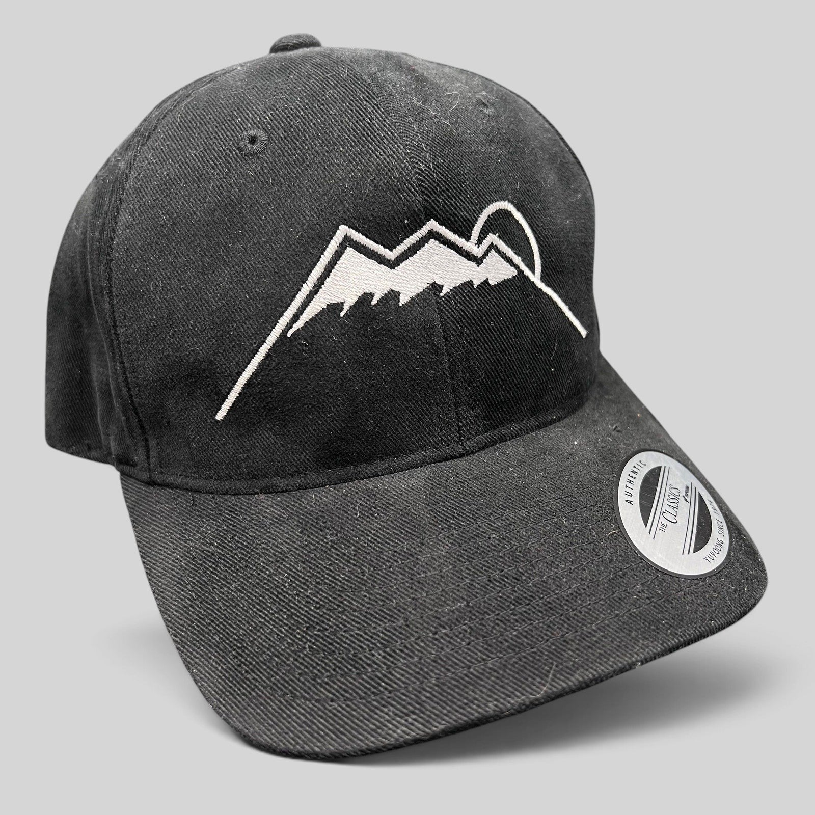 Raree Finds black Yupoong strapback hat featuring a white embroidered Humphreys Peak mountain and sun graphic.