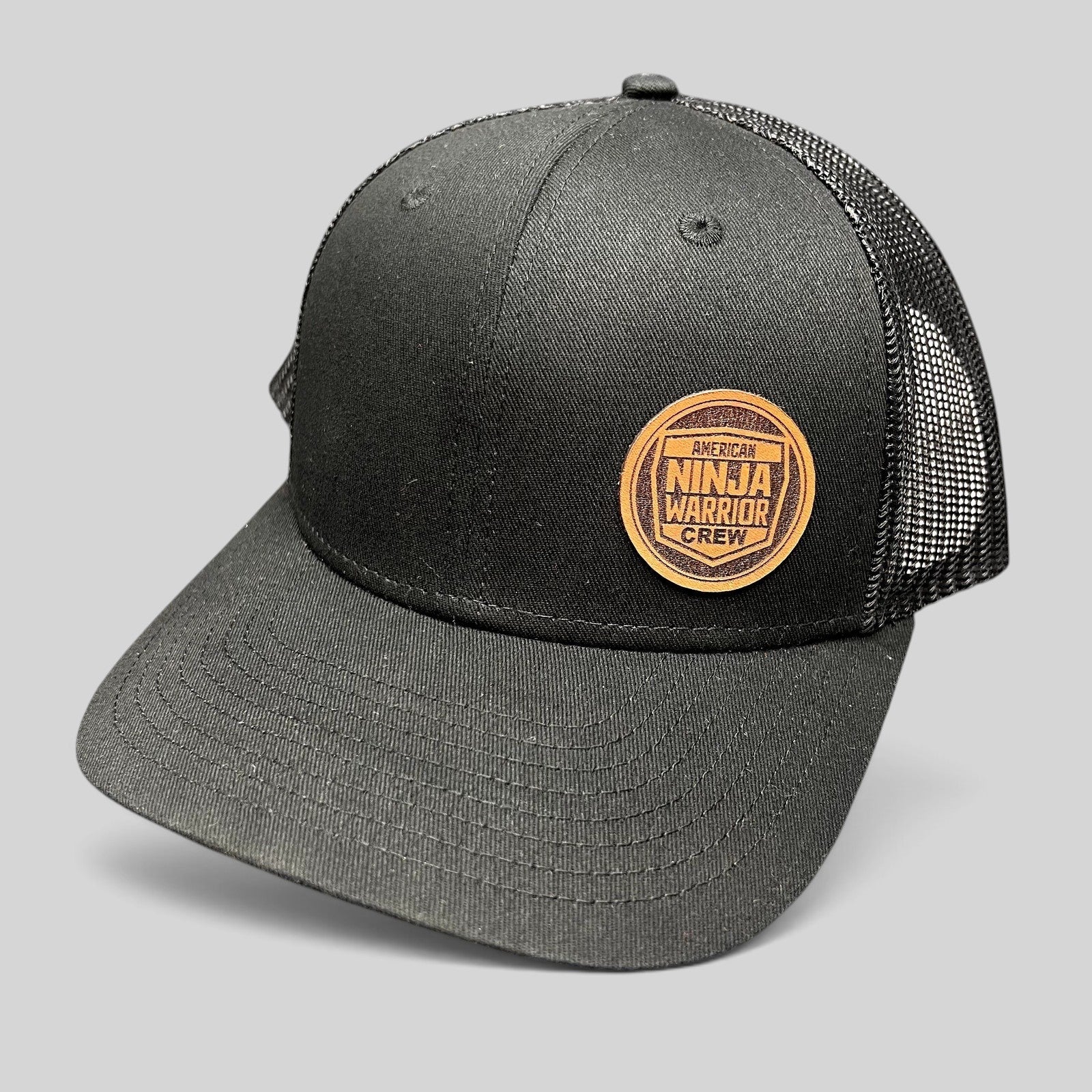 Raree Finds black American Ninja Warrior crew trucker snapback hat with a circular leatherette patch and mesh back.