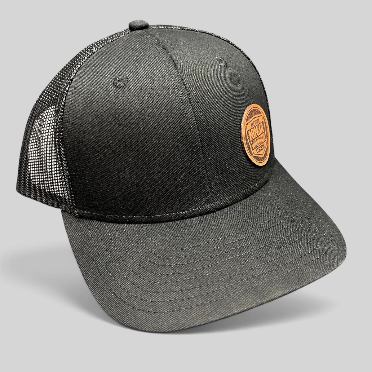 Raree Finds black American Ninja Warrior crew trucker hat with a circular leatherette patch and mesh back panels.