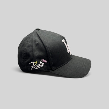 Raree Finds black Okami Brand strapback hat with white embroidered LV logo and side Foodie script detail