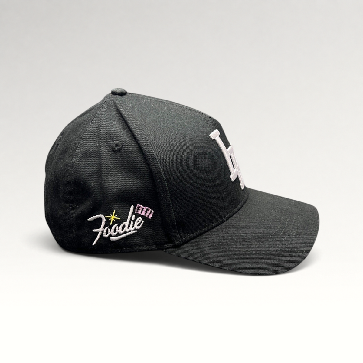 Raree Finds black Okami Brand strapback hat with white embroidered LV logo and side Foodie script detail
