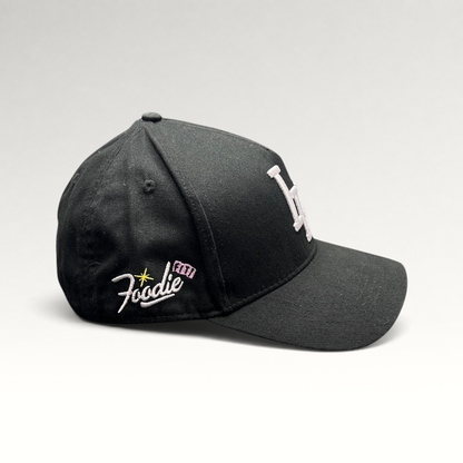 Raree Finds black Okami Brand strapback hat with white embroidered LV logo and side Foodie script detail