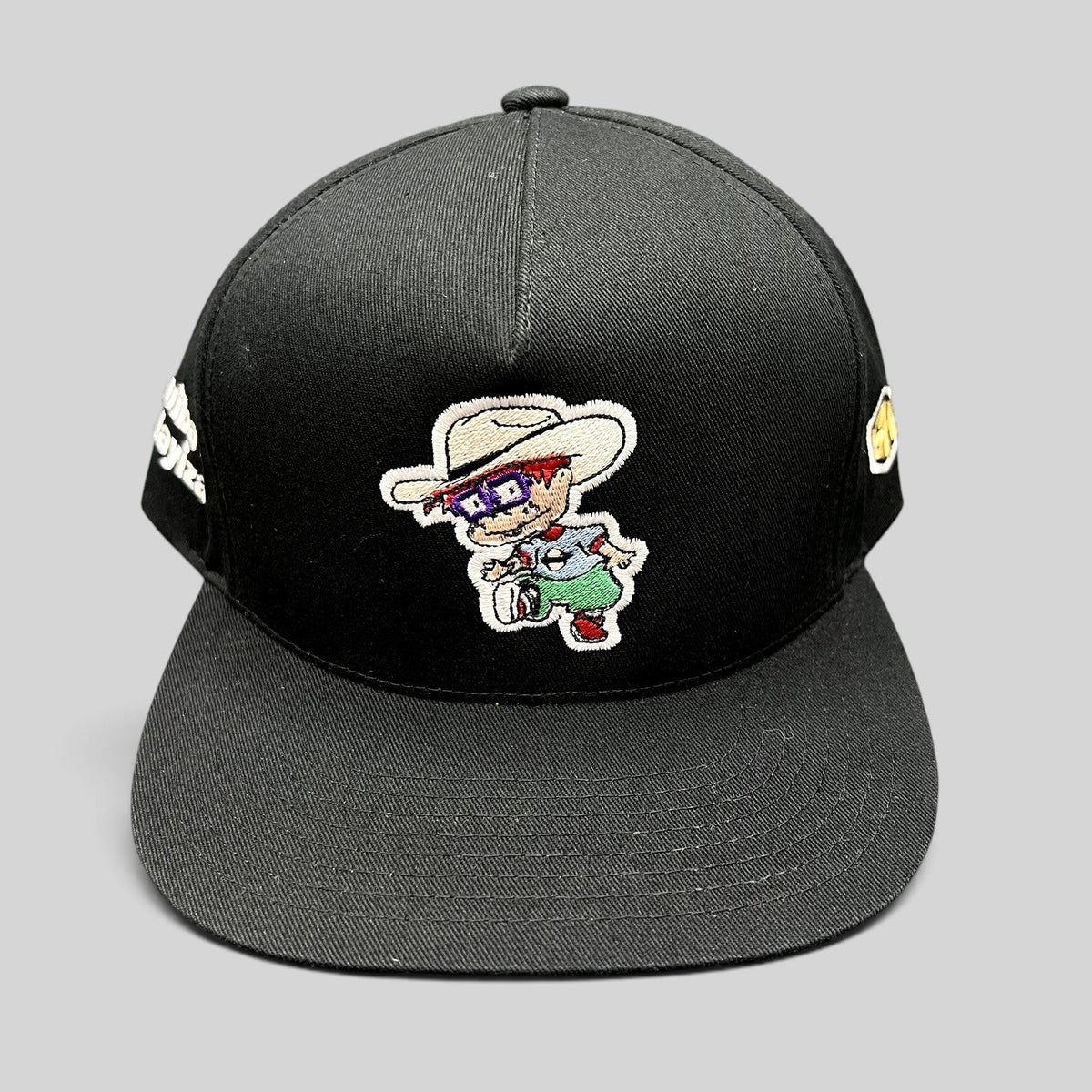 Raree Finds black Yupoong snapback hat with Rugrats-style embroidered character and flat brim design.