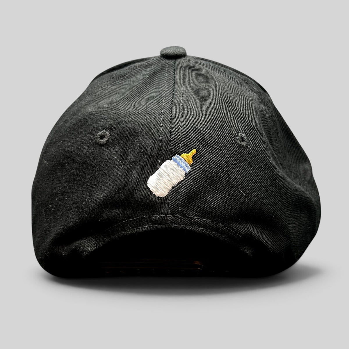 Raree Finds black Yupoong snapback hat featuring a small embroidered baby bottle graphic on the rear panel