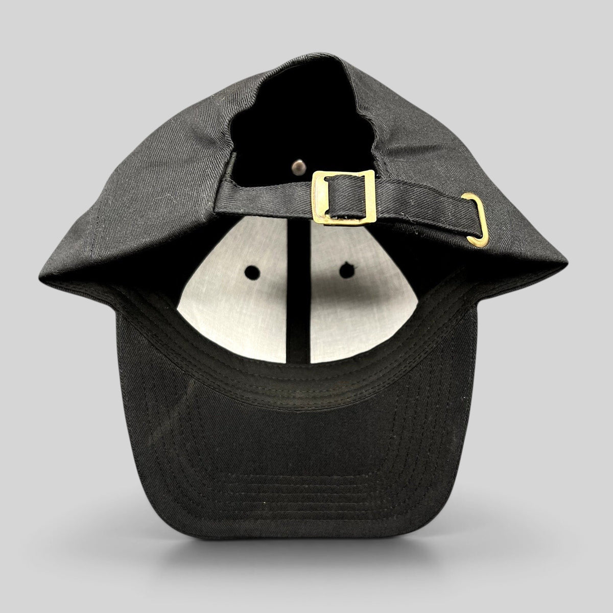 Raree Finds black cotton strapback hat with adjustable brass buckle closure, showing the interior and back view.